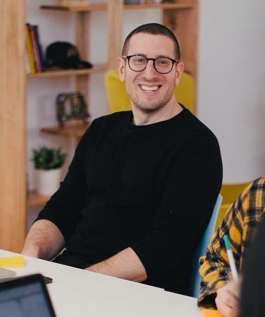 dark haired man with glasses sat at table smiling